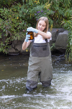 A woman stands in a river and closes a jar full of water