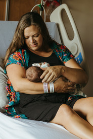 A woman sits on a hospital bed and looks at the newborn baby cradled in her arms