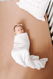 a baby wrapped in a white blanket lies in a crib with pink sheets