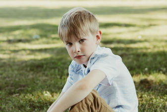 A six year old boy leans an arm on a bent knee as he sits on grass
