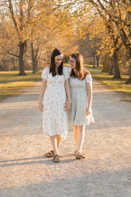 Two woman hold hands and walk down a path under trees