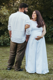 A man faces backwards while a pregnant woman faces forward and they link arms and look at each other