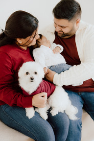 A man and woman looks down at a sleeping baby between them as a small white dog sits on the woman's lap