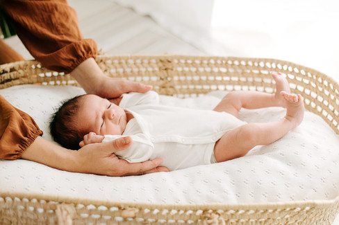 new born baby girl wearing a bow while sleeping in a Moses basket