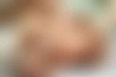 A newborn baby being dressed by two woman's hands into a pink onesie