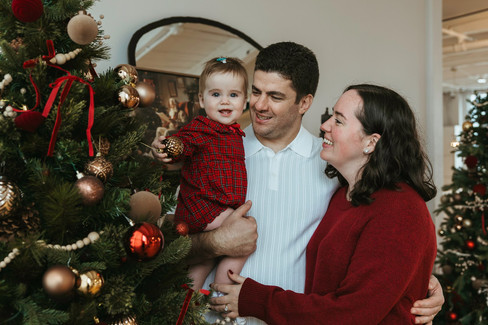 A man, woman and baby girl smile and look at a Christmas tree
