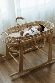 A newborn baby in a white onesie and black hair bow lies in a bassinet