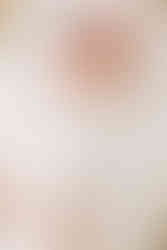 A newborn baby in a white onesie and pink hairband lies in a bassinet