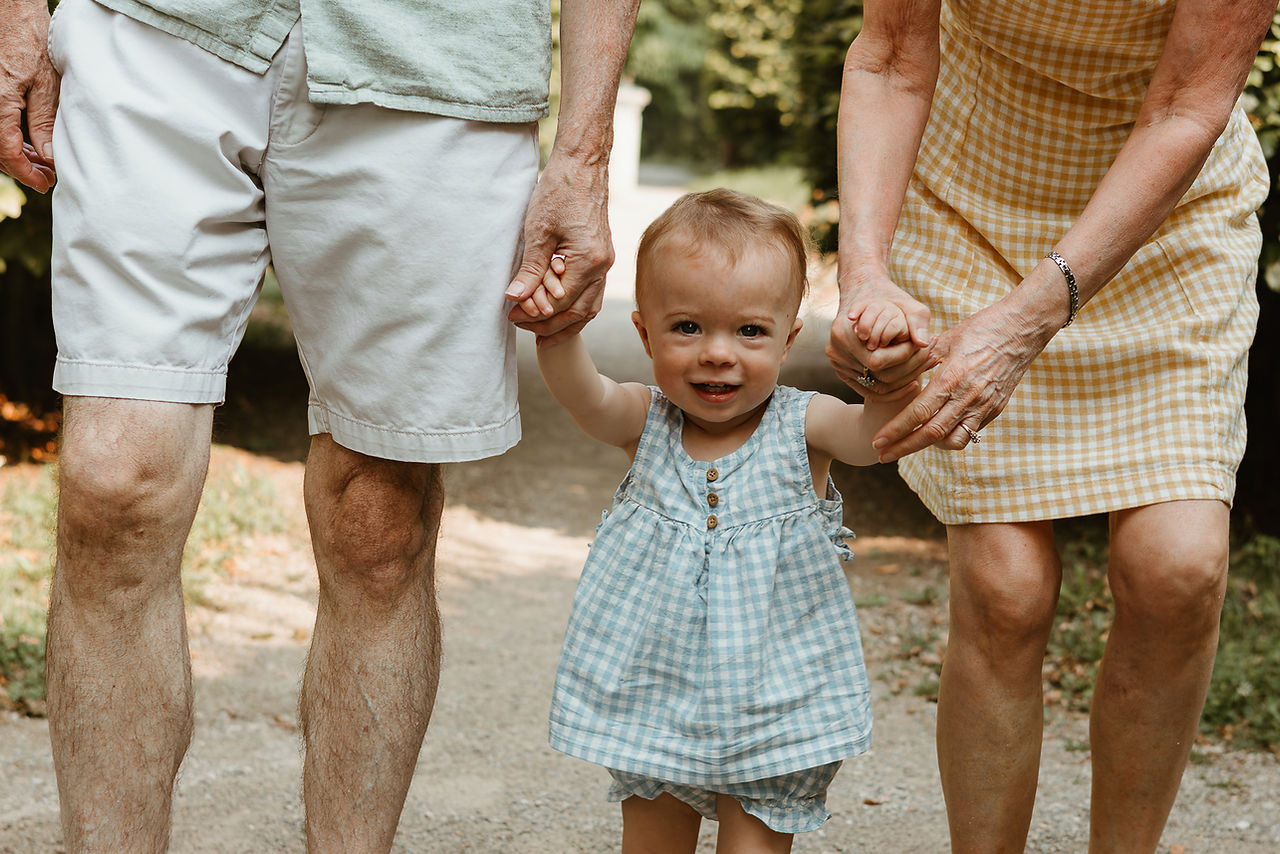 A toddler girl smiles as she holds hands with a woman and man