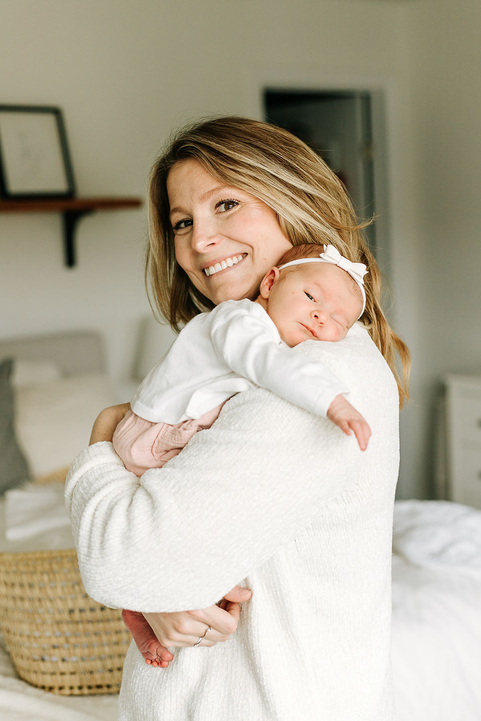 A woman dressed in white cradles a baby also dressed in white to her shoulder