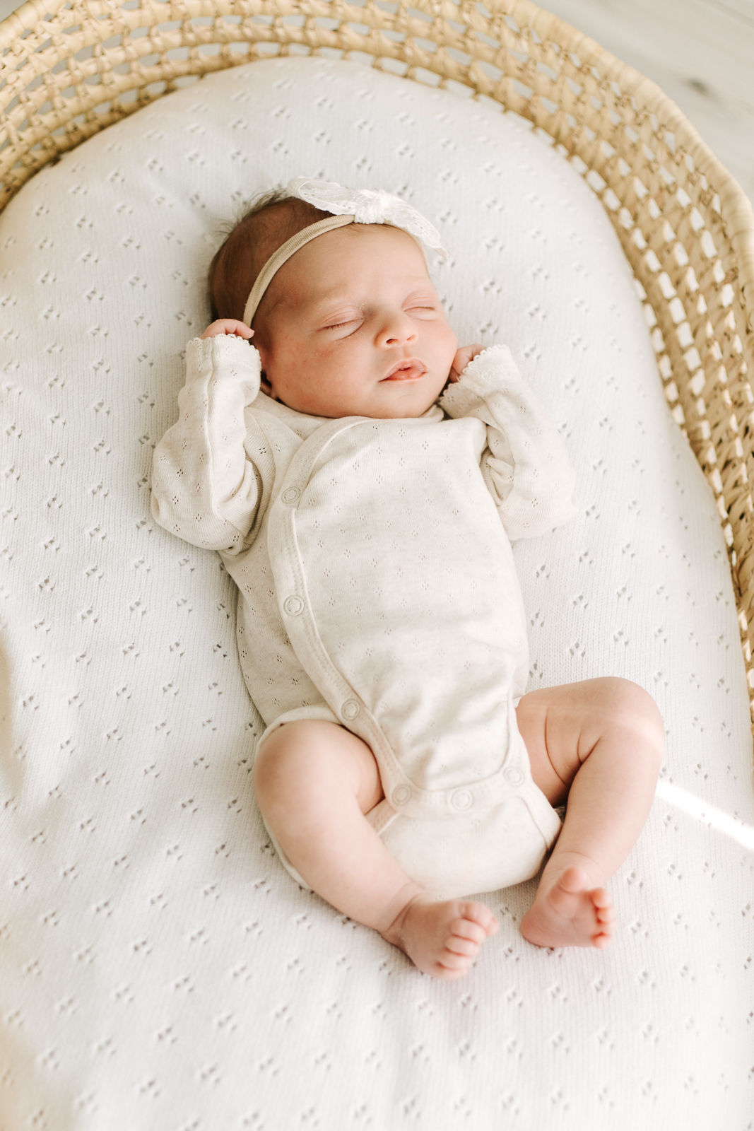 new born baby girl wearing a bow while sleeping in a Moses basket
