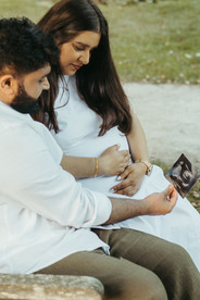 A pregnant woman and a man sit on a bench and look down at an ultrasound picture