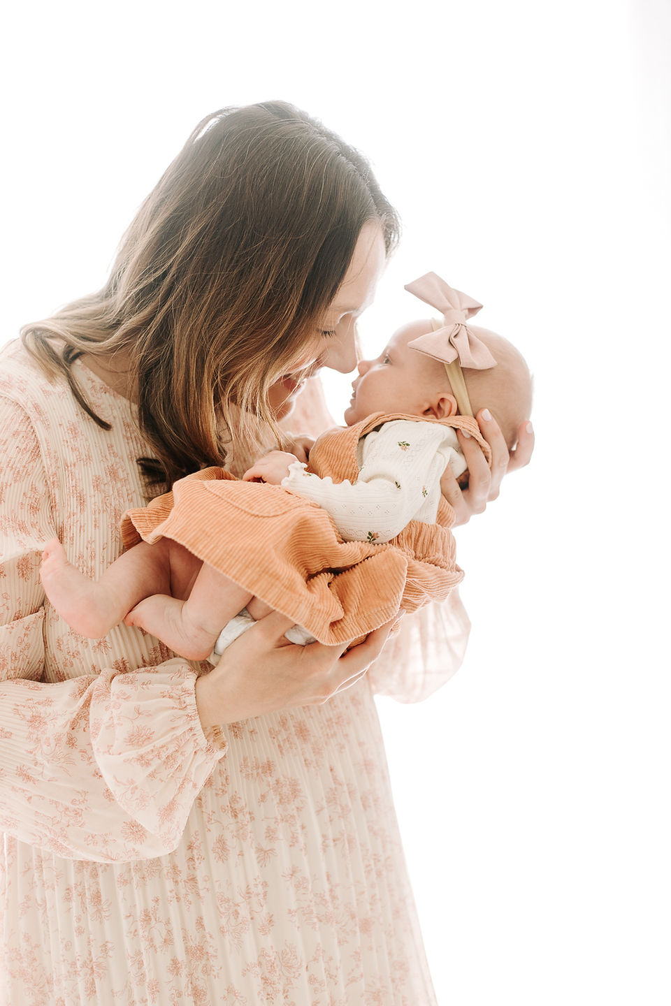 A woman in a floral dress holds a baby in her arms as they touch noses