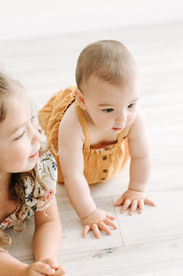 A six month old baby girl and a toddler girl crawl on the floor