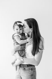 A woman holds a one year old girl in her arms and kisses her cheek