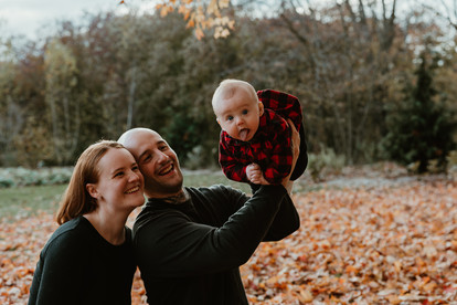 A man and woman smile as he holds up a baby in the air who is sticking out her tongue