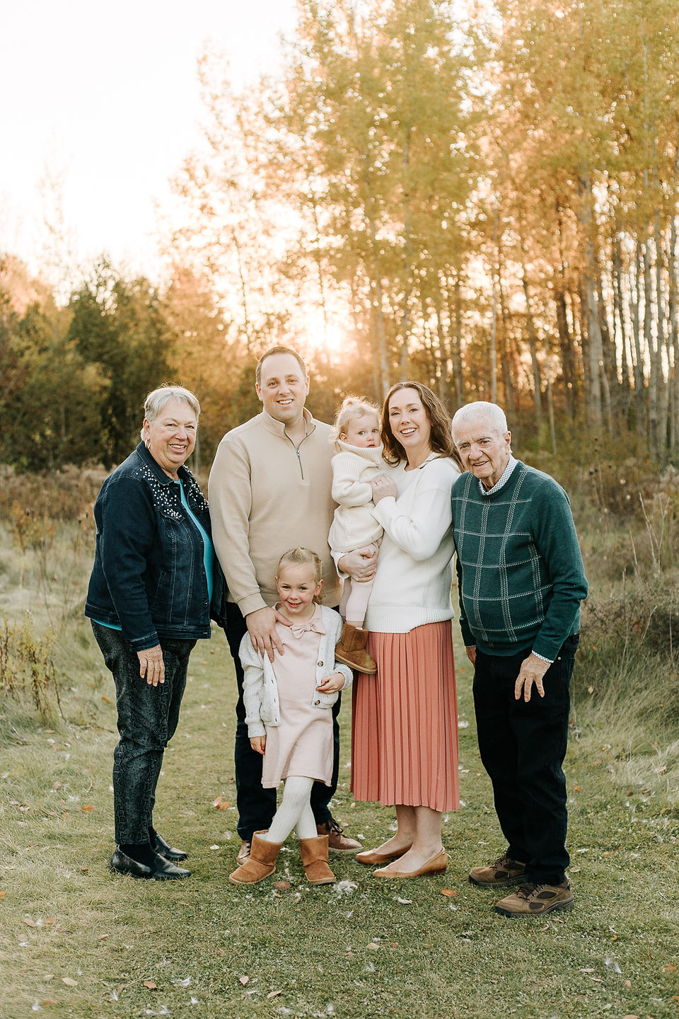 A couple stand and smile in a forest with two girls and an older couple