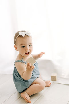 A six month old girl sits on the floor and plays with wooden blocks