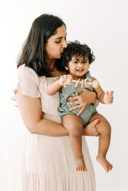 A one year old boy sits in a woman's arms as she kisses his head
