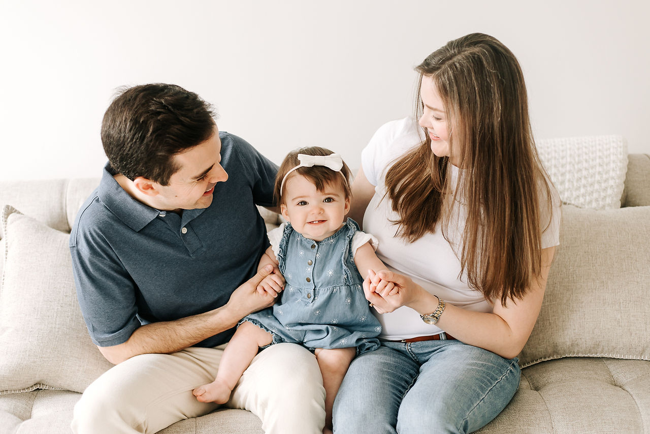 A man and woman hold a one year old girl between them and look down at her