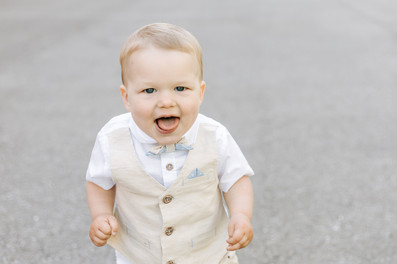 A toddler boy in a suit vest and bow tie sticks out his tongue