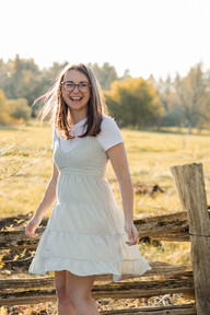 A woman twirls in a dress in front of a wooden fence