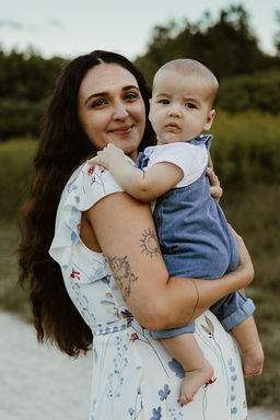 A woman smiles as she holds a baby in a grassy field