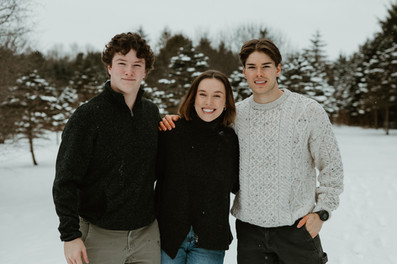 A young woman and two young men stand with their arms around each other smiling outside in the snow