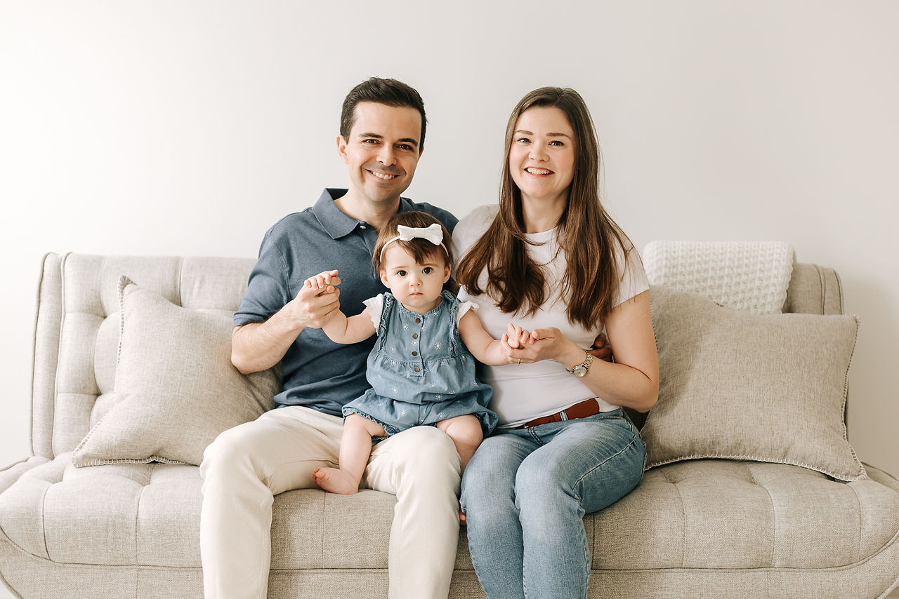 A man and woman sit on the couch with a one year old girl sits on their lap