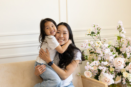 A woman a girl hug on a couch and beside them is a floral arrangement