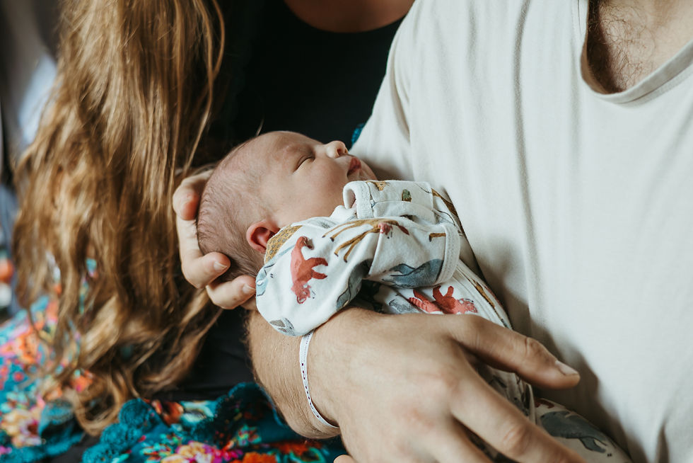 A newborn baby in a man's arms while a woman sits next to him and cradles the baby's head in her hand