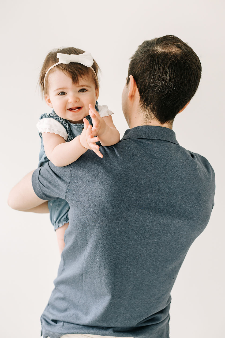 The back of a man in a navy blue t shirt with a one year old girl looking over her shoulder