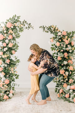 A woman and girl hug and smile with flowers behind them