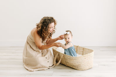 A woman kneels on the floor beside a six month old baby in a moses basket