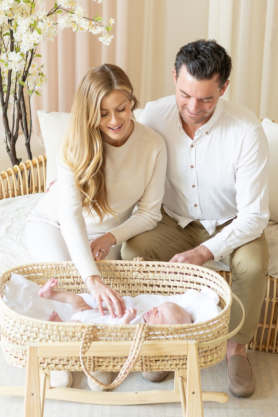 A man sits on a couch next to a woman who is looking down at a newborn baby in a bassinet