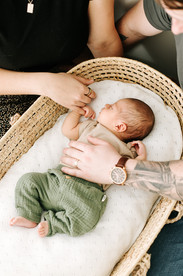 A newborn baby lays in a moses basket with a man and woman's hands on him