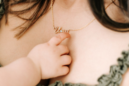 A baby's hand touches a woman's necklace that says Elora