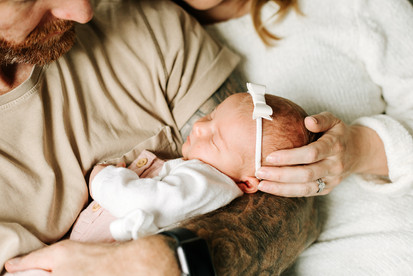 torso of a man in a tan t shirt and a woman in a white sweater while the man holds a baby and the woman rests her hand on the baby's head