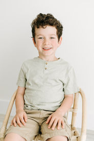 A young boy sits on a small rattan chair
