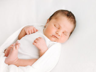 newborn baby boy in white onesie sleeps on a white sheet