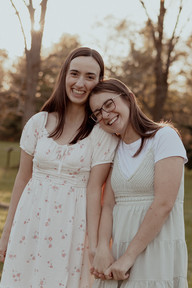 Two woman hold hands as one rests her head on the other shoulder