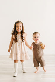 A one year old boy stands and holds hands with a young girl as they smile