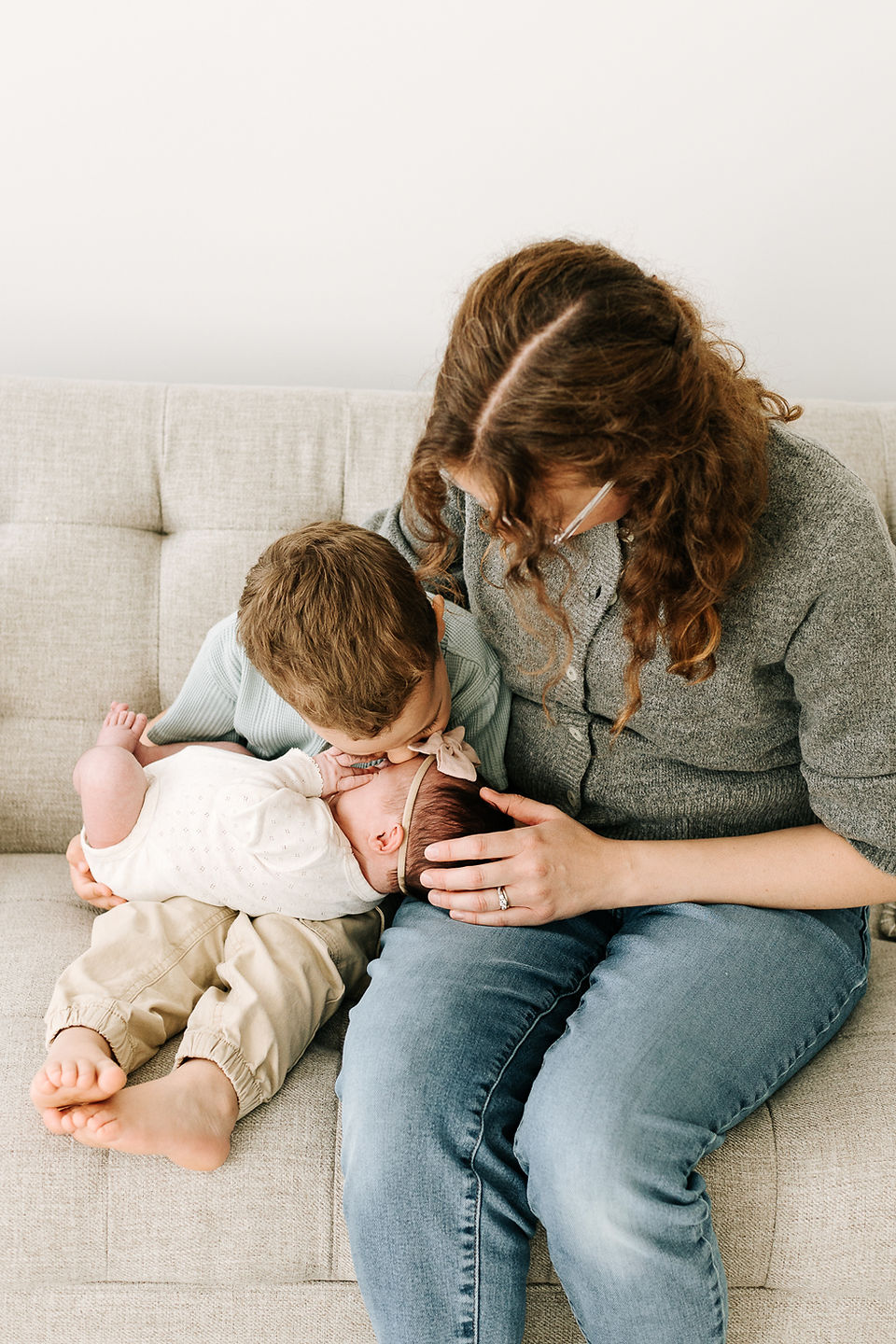 A woman sits on the couch while a young boy sits beside her and holds a newborn baby
