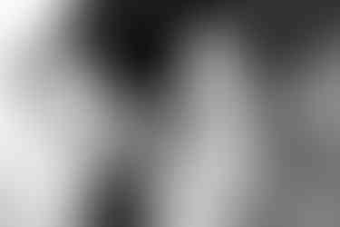 The torso of a man and woman as the man holds a newborn baby and a young boy stands in front of them and tickles the baby's feet