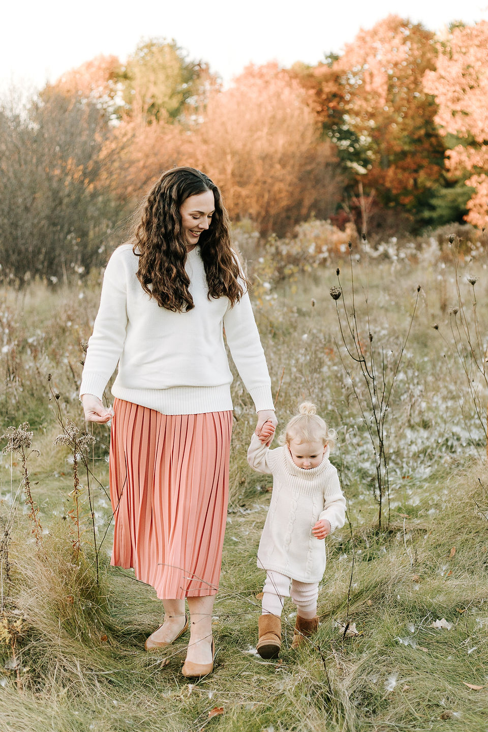 A woman walks hand in hand with a little girl on a grass path amongst trees in the fall
