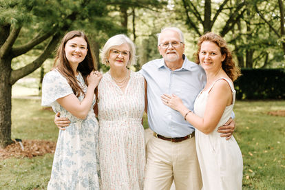 An older couple and two younger woman stand with their arms around each other