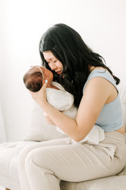 A woman sits on a couch and holds a newborn baby to her face