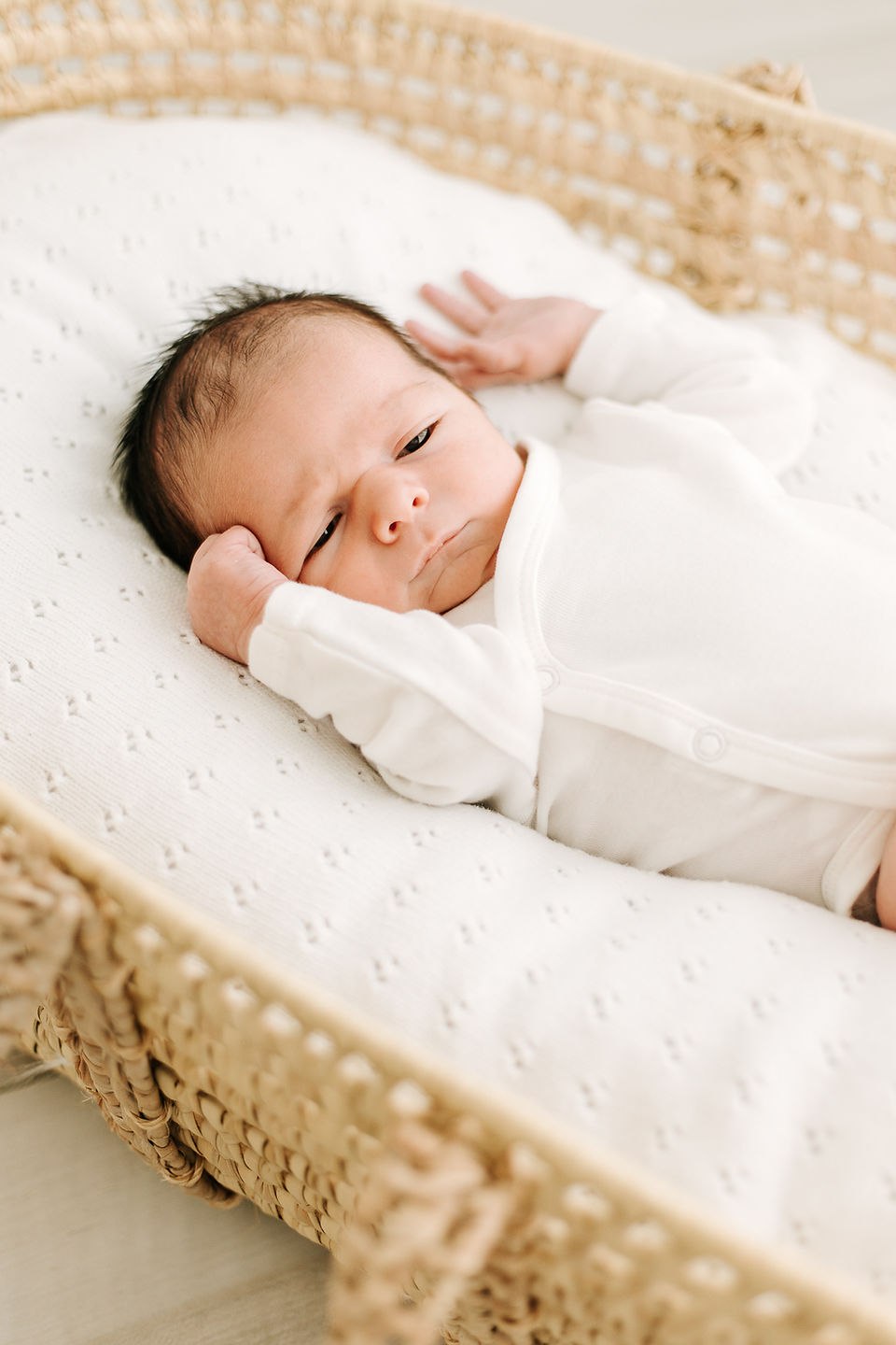A newborn baby in a white onesie lies in a bassinet