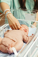 A woman reaches her hand into a bassinet and strokes the cheek of a newborn baby