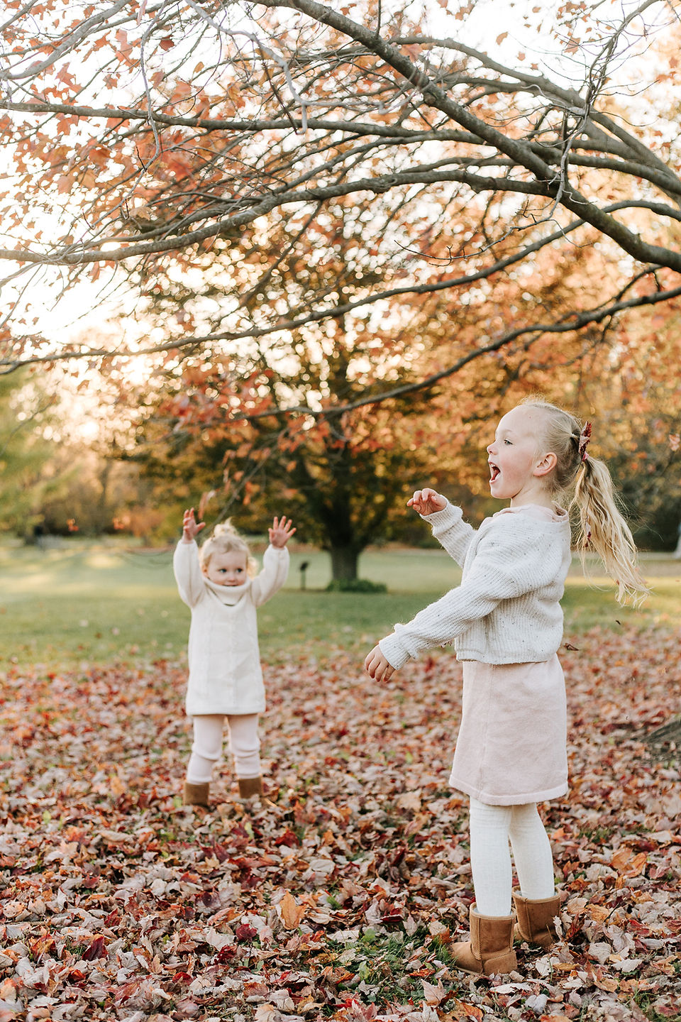 Two young girls play in the leaves in fall as the sun sets